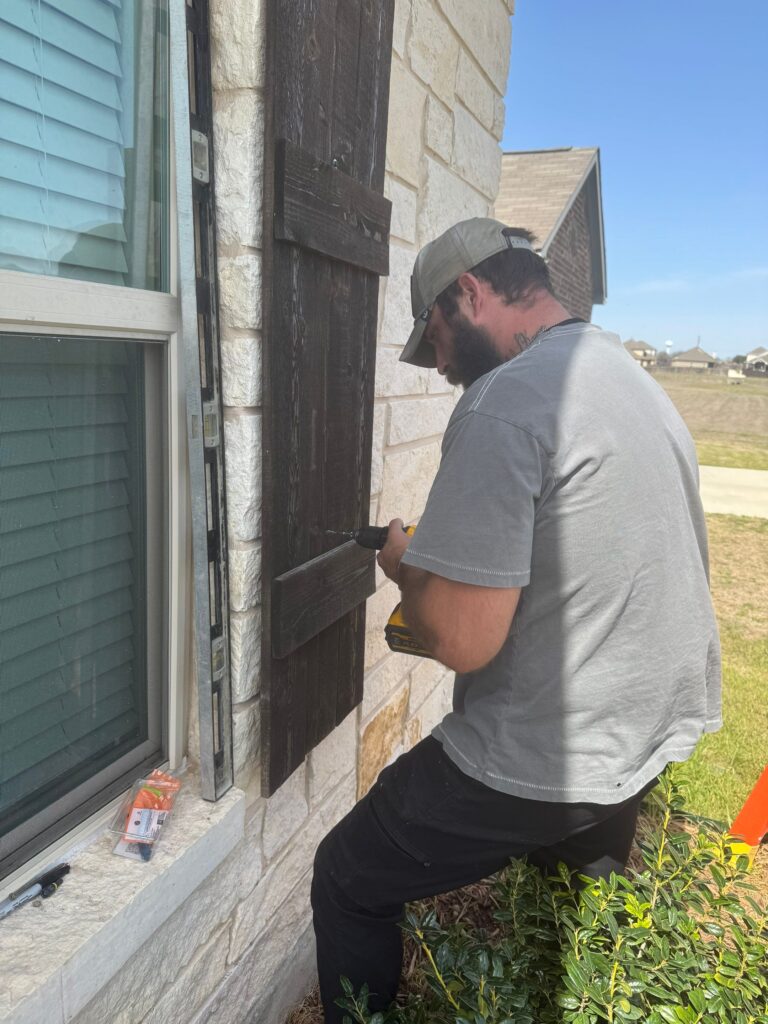 The Worker Is Installing Or Repairing Wooden Shutters Next To A Stone Wall And A Window ا